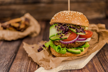 Tasty vegan burger with fresh vegetables on dark rustic wooden table, selective focus. Healthy fast food background with space for text.