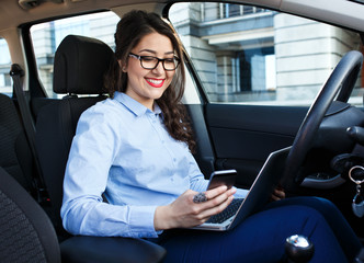 Beautiful young business woman using laptop and phone in the car.	