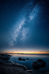 Beautiful view of milky way glowing on the sky with calm sea and a man looking at the stars and sunset