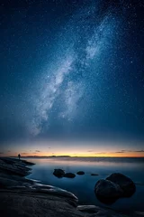 Fotobehang Prachtig uitzicht op de Melkweg die aan de hemel gloeit met kalme zee en een man die naar de sterren en de zonsondergang kijkt © Jamo Images