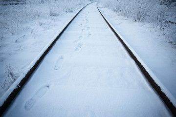 Railroad tracks in winter with foot steps on snow leading forward