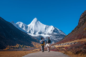 Male and female traveller at Yading Nature Reserve, Daocheng county, Ganzi Tibetan Autonomous Prefecture, Sichuan province of China. The holy peak Yangmaiyong (Jampelyang) can been seen in the backgro - obrazy, fototapety, plakaty