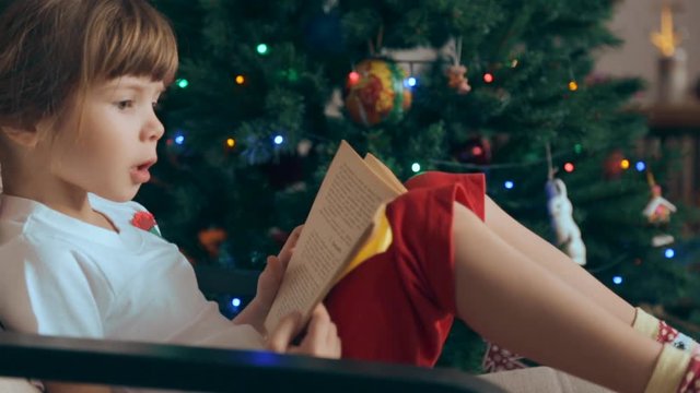 Small girl reading a book in front of Christmas tree