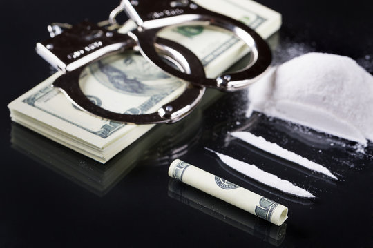 Handcuffs on stack of dollar banknotes and cocaine