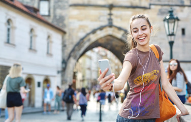 a young smiling woman tourist in sportswear walking in the center of Prague with a phone and taking photo and selfie. travel guide, tourism in Europe, woman tourist with smartphone on the street