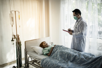 Doctor writing on clipboard while looking at patient in hospital.