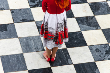 Girl with red hair and in a dress with a red pattern of London symbols on the chess floor.