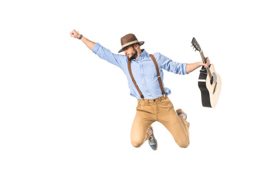 young musician in hat holding guitar and flying with raised hand isolated on white