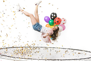 smiling girl holding colorful balloons and falling on trampoline isolated on white