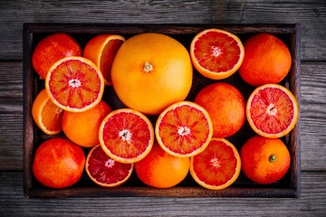 Sliced and whole ripe juicy blood oranges and grapefruit in the box on wooden background.