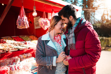 Couple in love standing on the street, smiling and buying some sweet lollipops. Anniversary, Valentine's day.