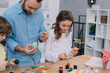 father and children painting eggs for easter holiday