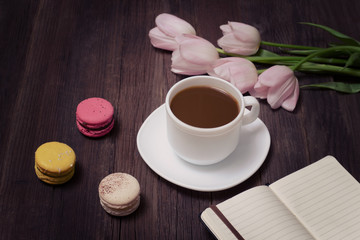 Fototapeta na wymiar Cup of tea, macarons, pink tulips and notebook on wooden background.