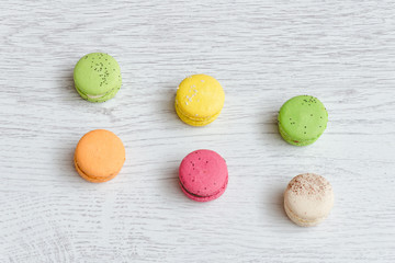 Six multicolored macarons on a light wooden table. Top view