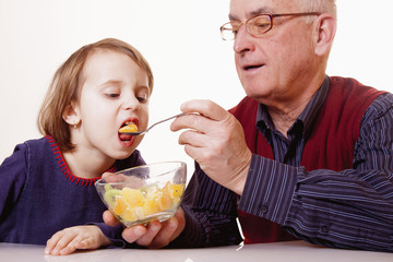 Grandpa feeding his grandchild with fruits salad.