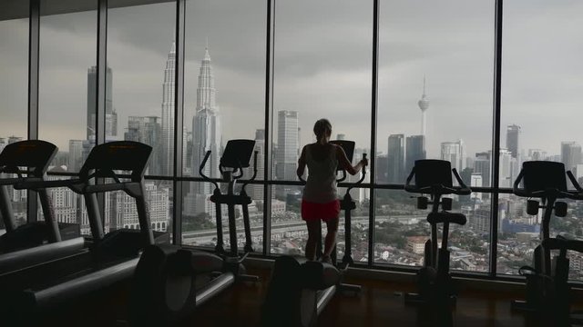 Slow motion shot of attractive young woman running on a treadmill in fitness sport club with beautiful city view.Active lifestyle concept.