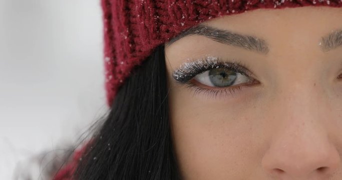 Close-up woman's green eyes blinking with snow on big eyelashes