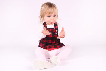 Little blonde toddler girl with big Blue Eyes in red  dress looking down.  Sitting on the floor, white background. Portrait, close-up isolated 