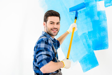 smiling handsome man painting wall with blue paint