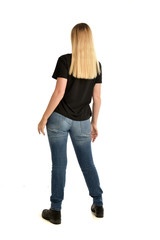 full length portrait of blonde girl wearing simple black shirt and jeans, standing pose wit back to...