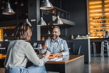 Handsome Caucasian middle-aged smiling man enjoying dinner at restaurant with a woman.