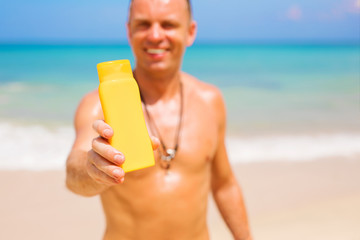 Man holding sunscreen bottle on the beach. Focus on the sample product bottle.