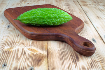 Fresh bitter melon or bitter gourd (Momordica charantia) on wooden cutting boards over pine wood grain