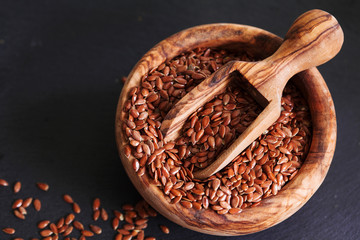 Organic flax seed in wooden bowl on black slate background copy space. Linum usitatissimum