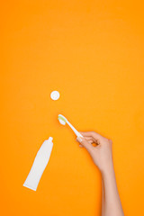 cropped view of woman holding toothbrush and tube of toothpaste, isolated on orange