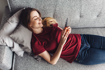 Girl using phone while lying on sofa at home
