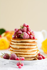 Stack of pancakes with raspberry, red currant, cream and honey on white table cloth