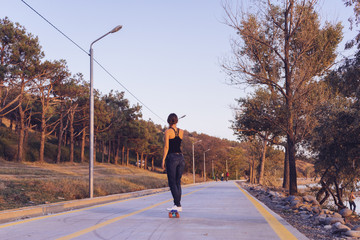 Fototapeta na wymiar active young girl is riding a longboard on an empty road