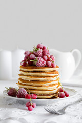 Stack of pancakes with raspberry, red currant, cream and honey on white table cloth