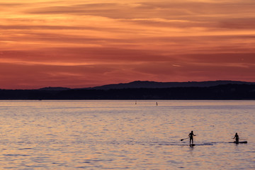 Couple paddleboarding into the August sunset, Bodensee, Germany