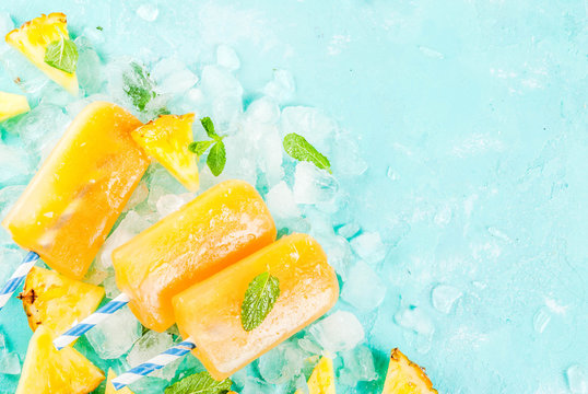 Homemade Pineapple Popsicles on Ice with fresh Pineapple slices and mint, on light blue background copy space
