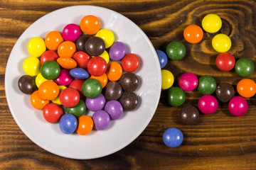 Saucer with colorful button shaped candies filled with chocolate on wooden table