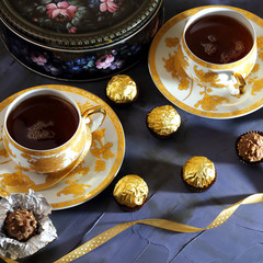 Tea ceremony. Two tea cups of gold color with black tea, candy, chocolate, box with biscuits.