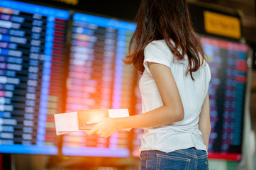  girl in international airport with passport and boarding pass near flight information board
