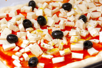 Raw pizza decorated mozzarella, black olives and tomato sauce