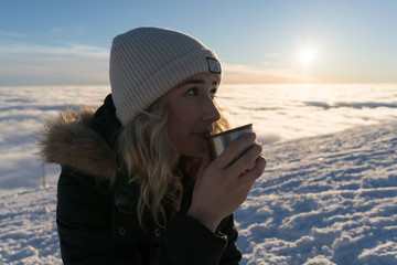 Girl drinking tea on snow in Slovak mountains above clouds during sunset in winter - 190228879