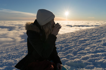 Girl drinking tea on snow in Slovak mountains above clouds during sunset in winter - 190228898