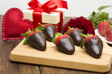 Fresh strawberries dipped in dark chocolate, gift and heart on wooden background. Valentine's Day.