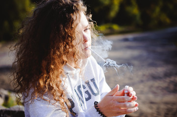 lovely young woman with curly hair, the romance of youth, a journey walk on a warm summer sunny day smokes a cigarette