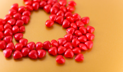 Heart traced with little red cinnamon candy in form of heart on an orange background