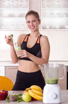Girl holding bottle with green smoothie in kitchen