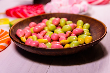 Ceramic plate with colored candies, lollipops and marshmallows on a wooden table