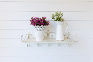 Two vases of flowers on shelf with white wall in background.