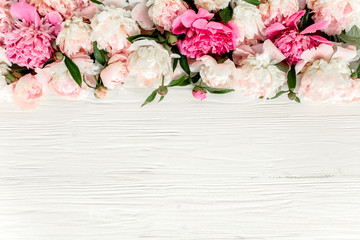 Floral frame made of pink and red peonies flower buds, branches and leaves isolated on white wooden background. Flat lay, top view. Frame of flowers. Floral background.