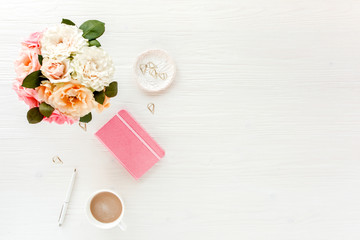 Fototapeta na wymiar Flat lay home office desk. Female workspace with pink and beige roses flowers bouquet, coffee and chocolates on white wooden background. Top view feminine background.
