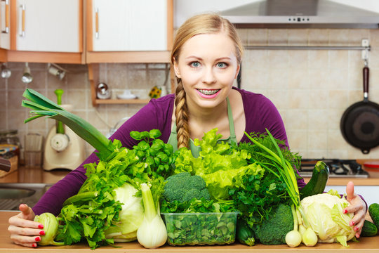 Smiling woman in kitchen with green vegetables